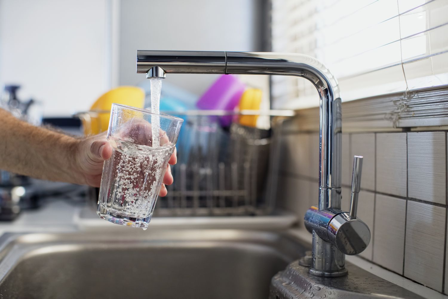 Person füllt ein Glas mit Wasser an einer Küchenspüle auf