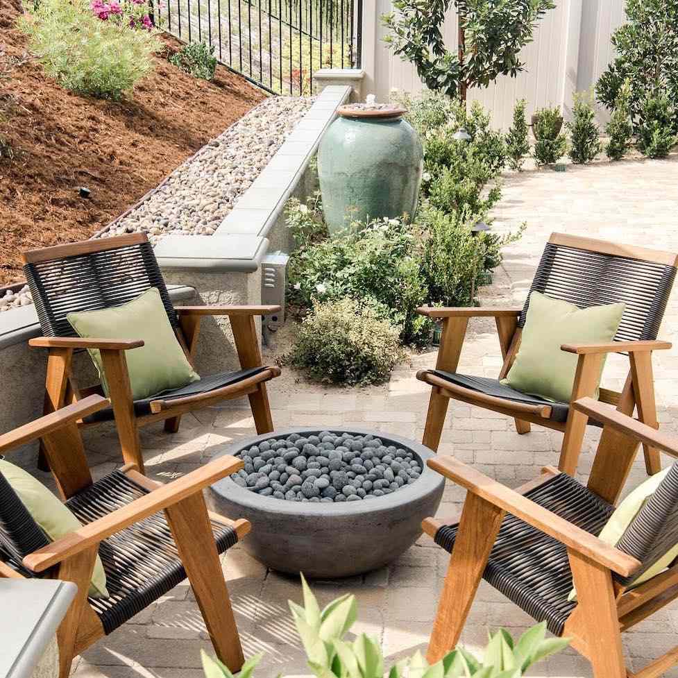 Tigela de pedra para fogueira com quatro cadeiras de madeira com plantas verdes e detalhes em um jardim deserto