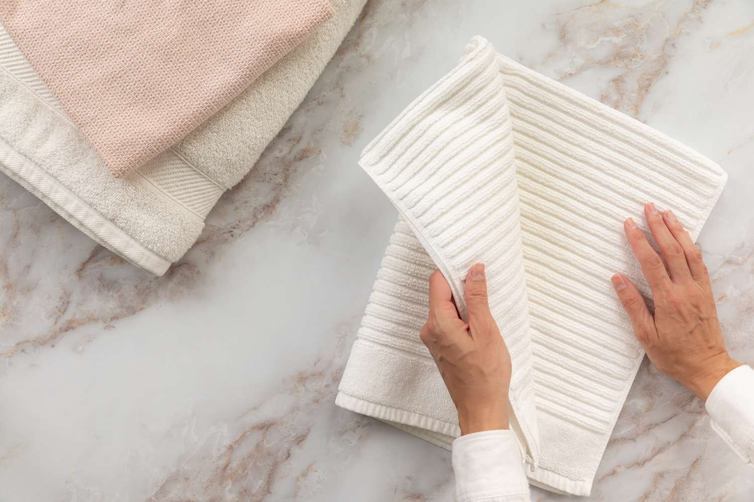 Toalla de baño blanca acanalada doblada por la mitad dos veces junto a otras toallas de baño