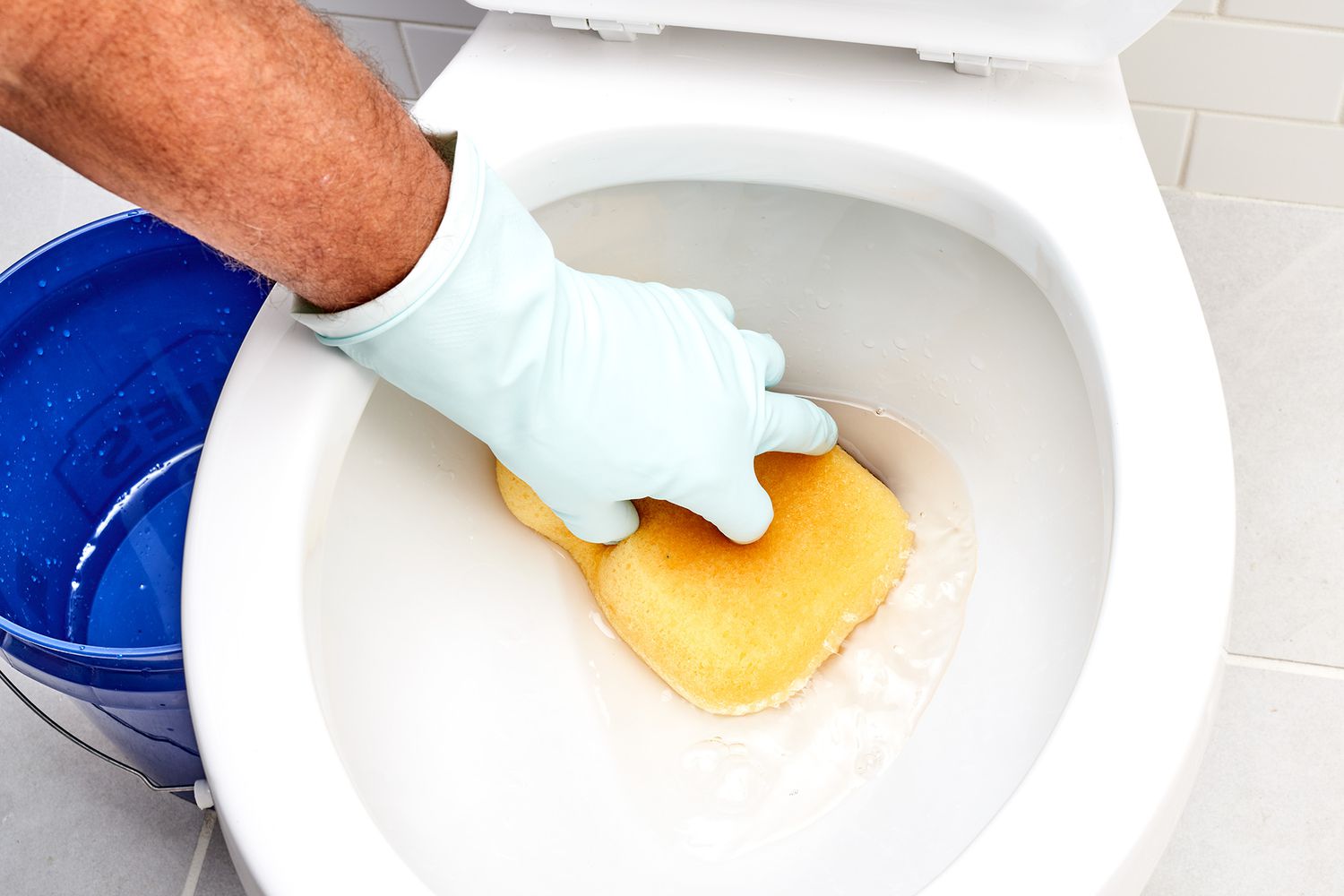 Wasser in der Toilettenschüssel mit gelbem Schwamm und Eimer mit Handschuhen entfernt
