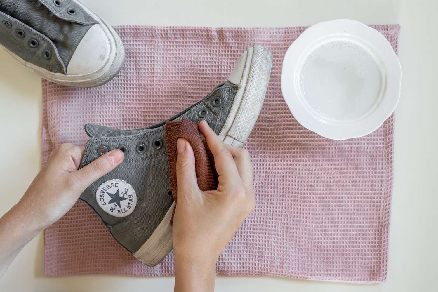 Mikrofasertuch, das die Außenseite des Converse mit einer Lösung aus Reinigungsmittel und Wasser abwischt