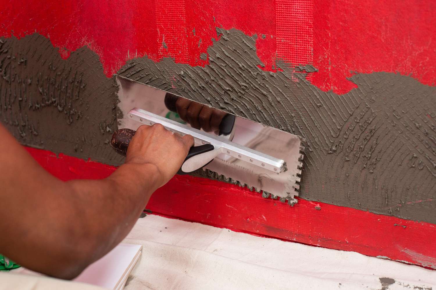 Adesivo de azulejo de fixação fina aplicado à parede vermelha com 