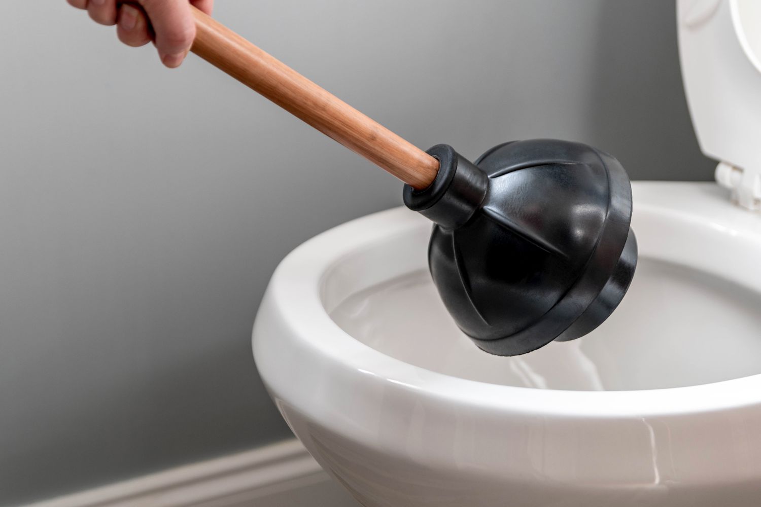 Black toilet plunger angled above toilet bowl