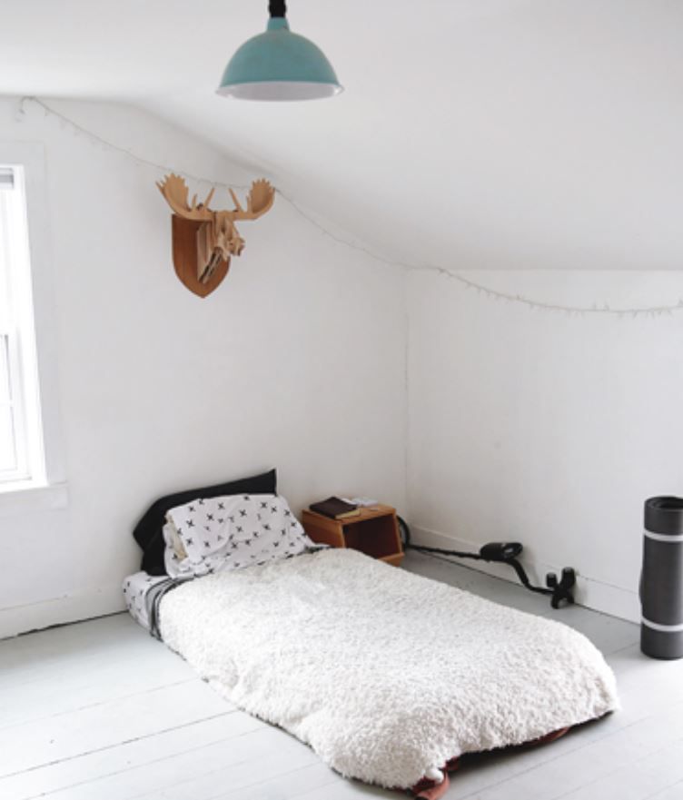 Chambre de garçon avec murs blancs et lit jumeau au sol.