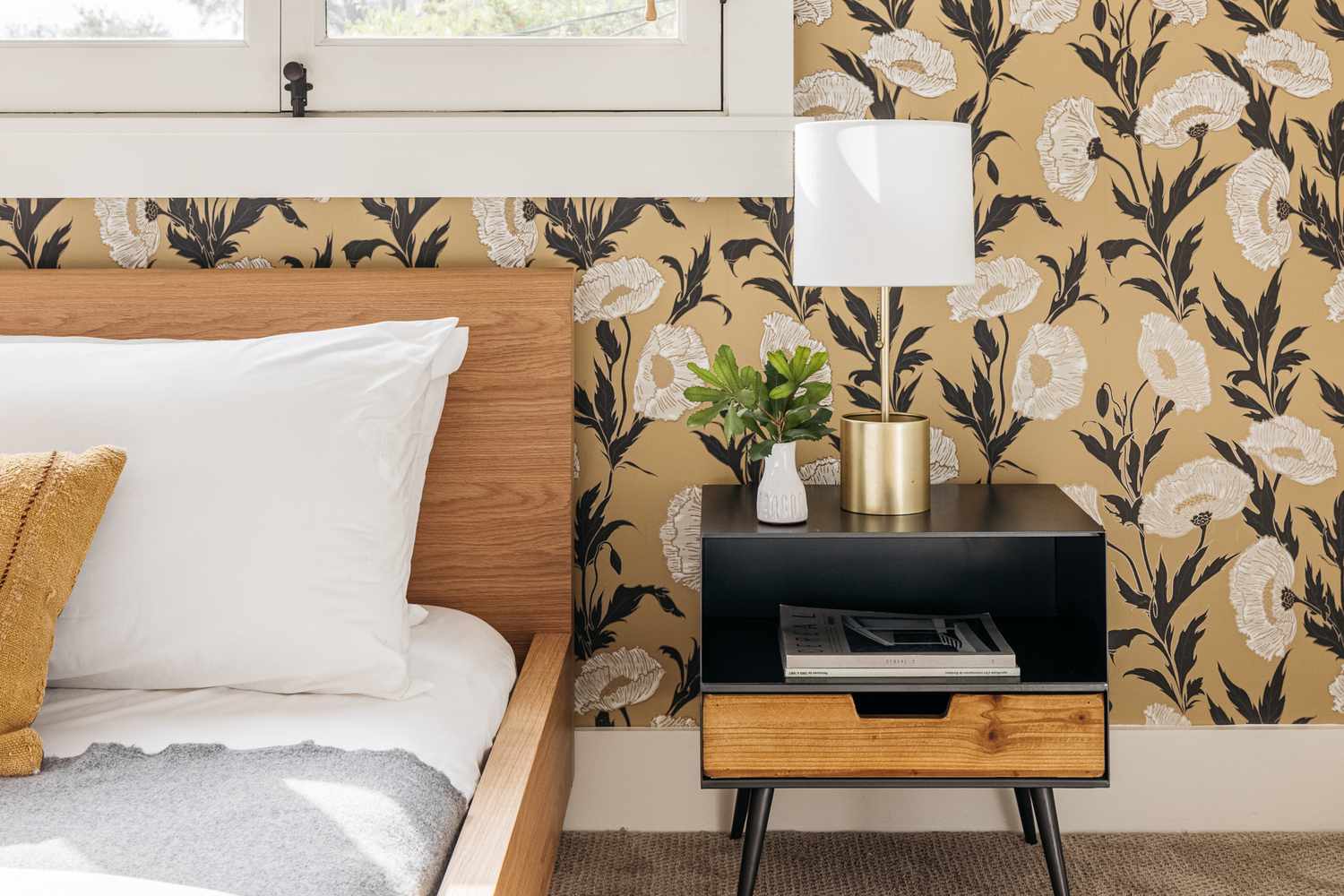 Chambre à coucher décorée avec papier peint floral, table de nuit noire et bois et cadre de lit en bois avec linge blanc
