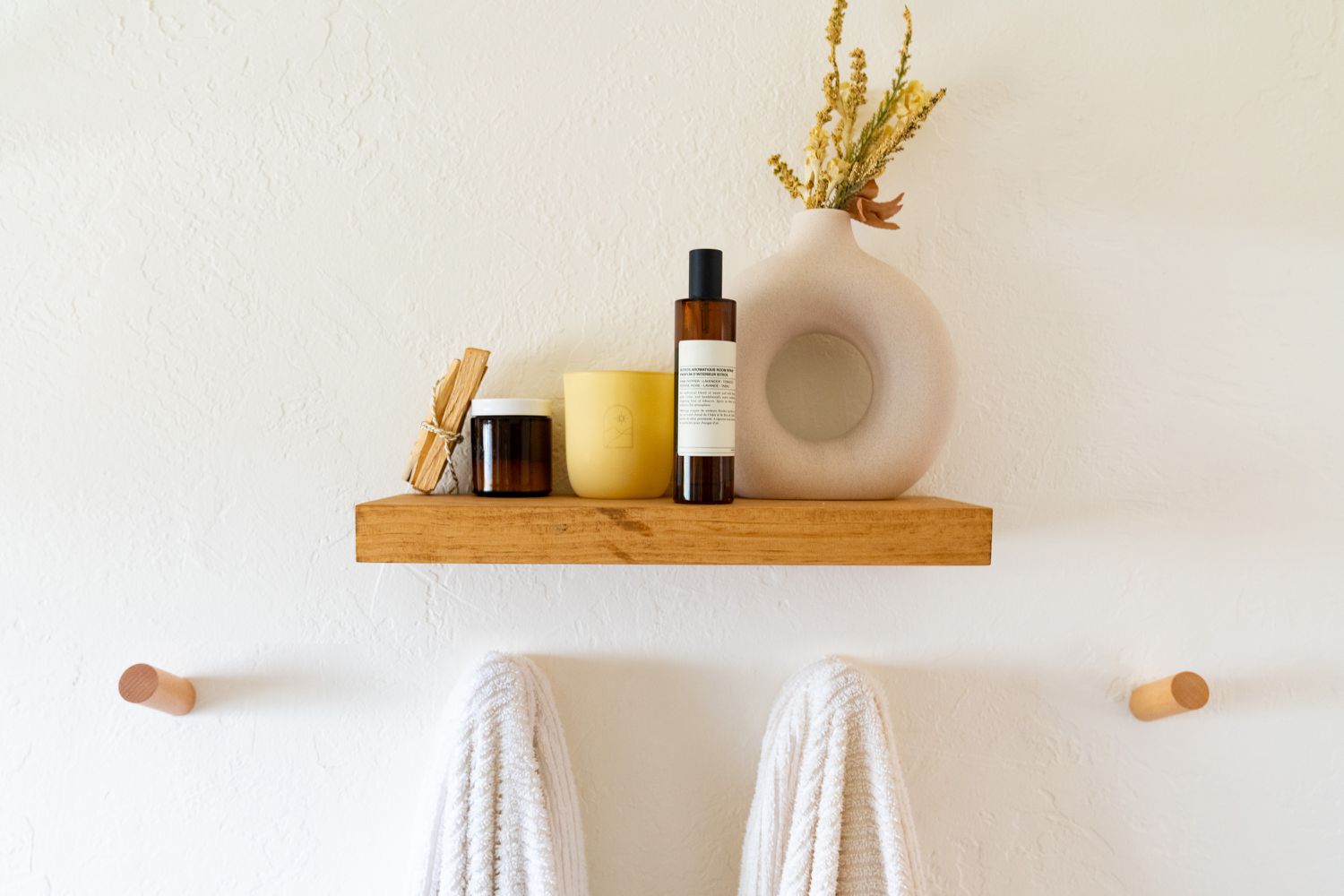 Kleines Holzbadezimmerregal mit Gegenständen oben drauf und Holzklammern, an denen Handtücher hängen