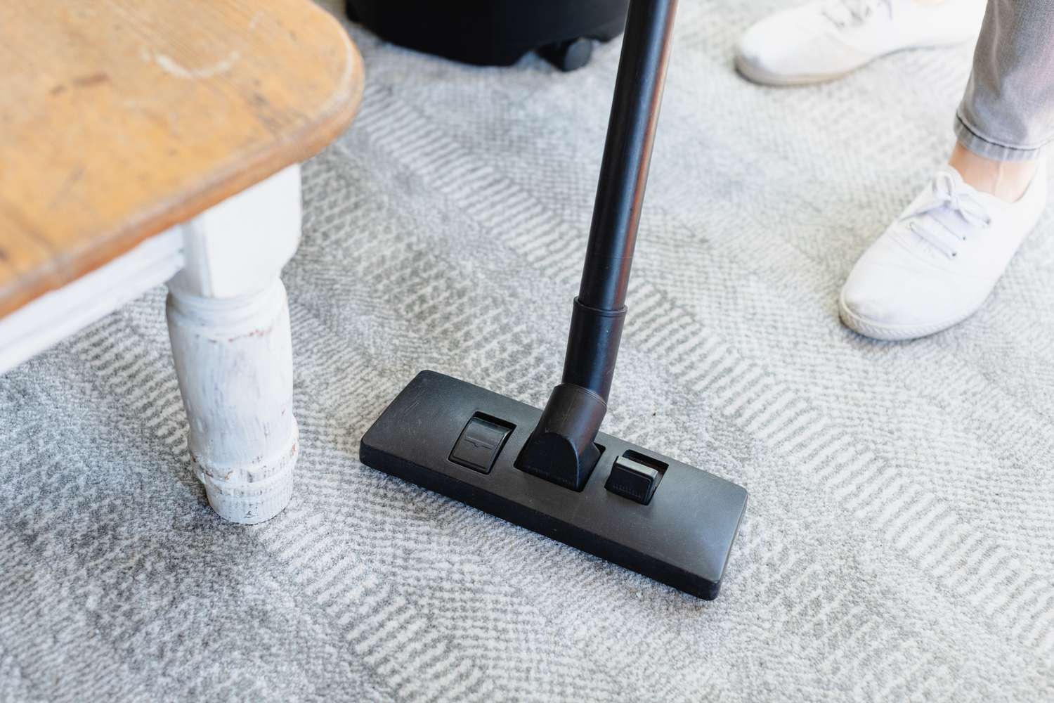 Aspirador de pó vertical limpando carpete ao redor da perna da mesa