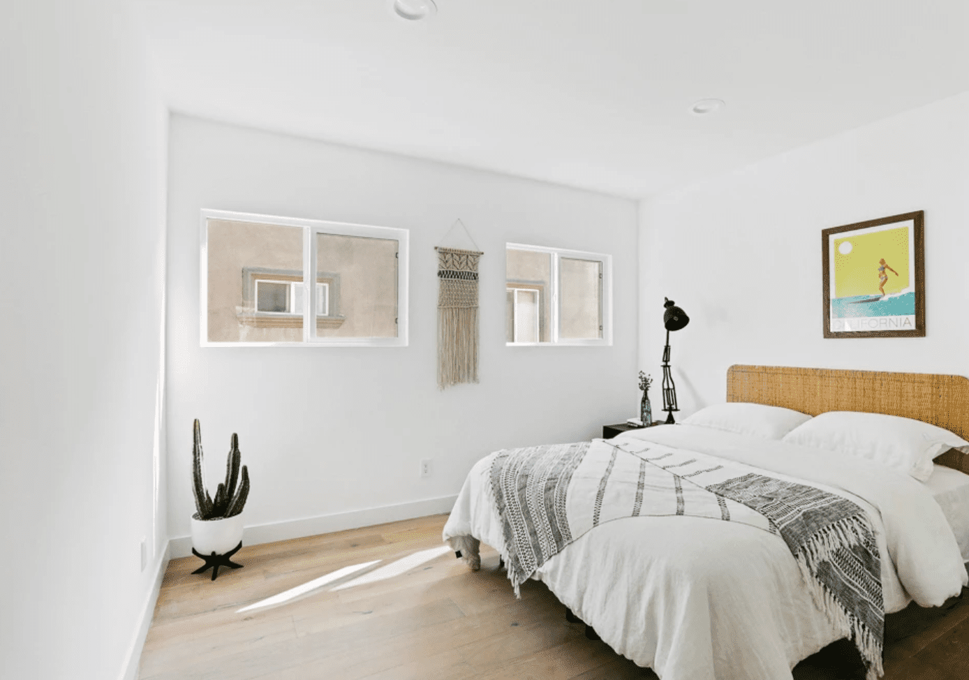 Ein California Cool-Schlafzimmer mit weißen Wänden, vom Strand inspirierten Drucken und einem geflochtenen Kopfteil