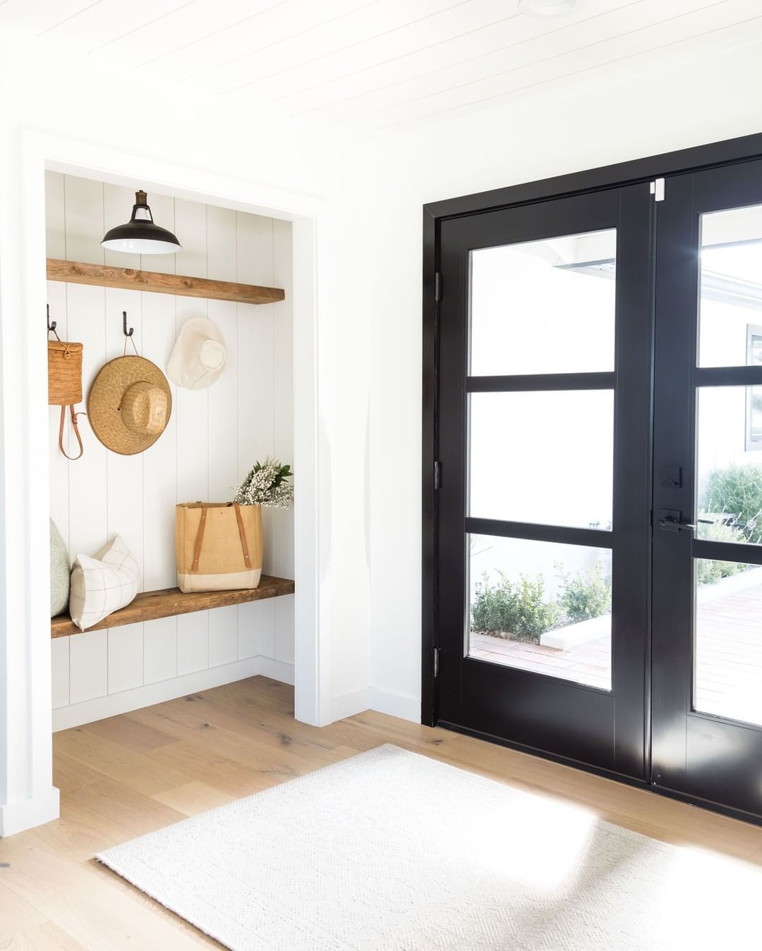 Un armario mudroom fuera de una entrada con paredes blancas, estanterías de madera abierta y sombreros colgantes.