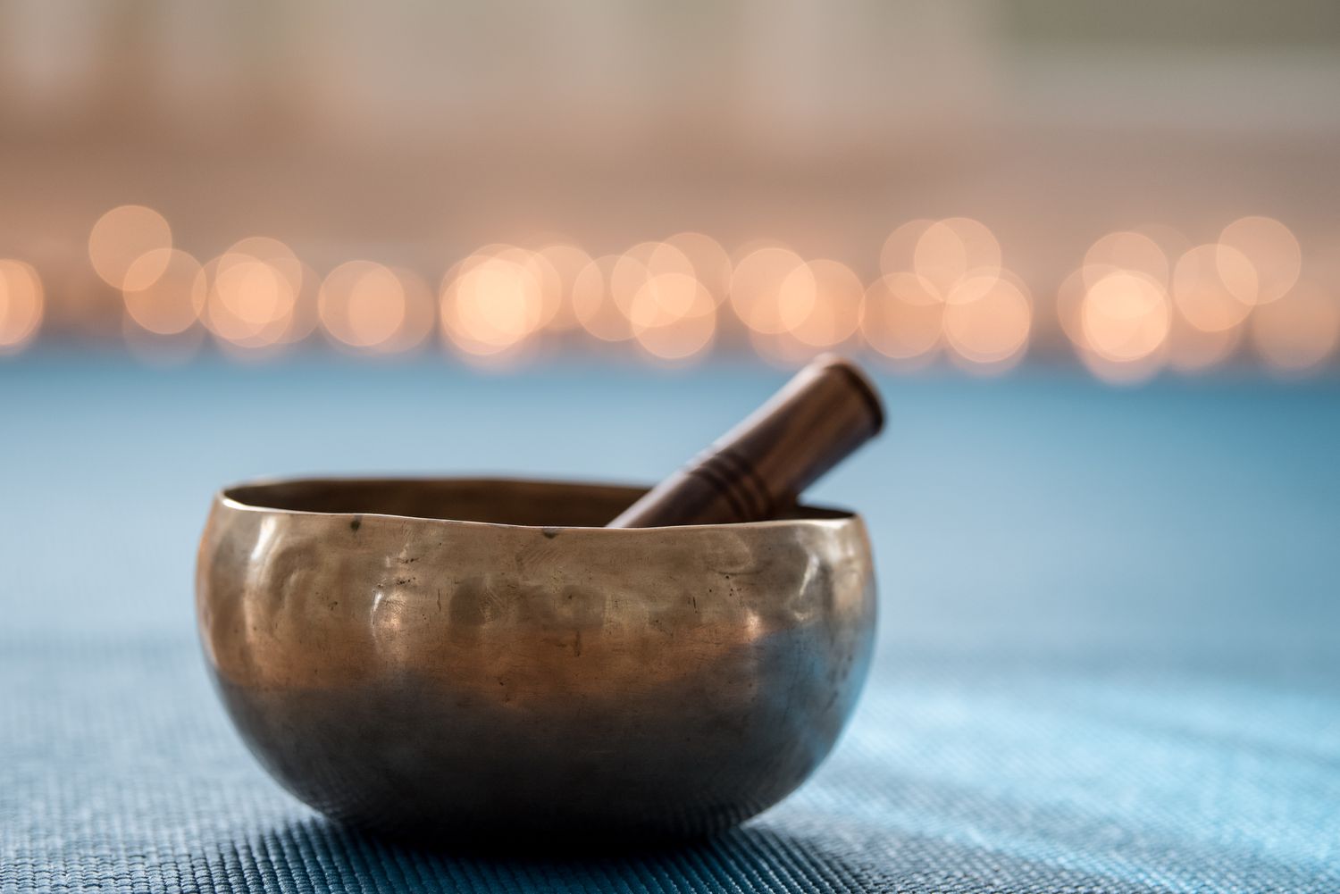 Tibetische Klangschale (Musikinstrument) auf Yogamatte mit Lichtern im Hintergrund