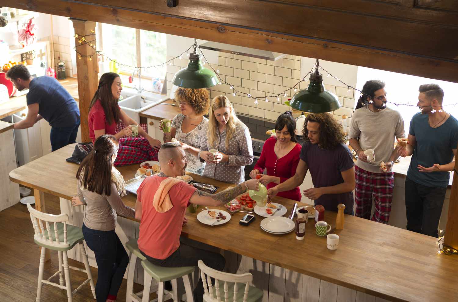 Eine Gruppe von Freunden bereitet in der Küche das Frühstück vor, sie essen Schinkensandwiches und unterhalten sich fröhlich. Es sieht aus, als wären sie auf einem Wochenendausflug.