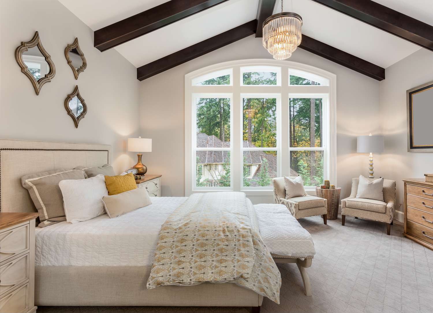 Master bedroom in new luxury home with chandelier and large bank of windows with view of trees