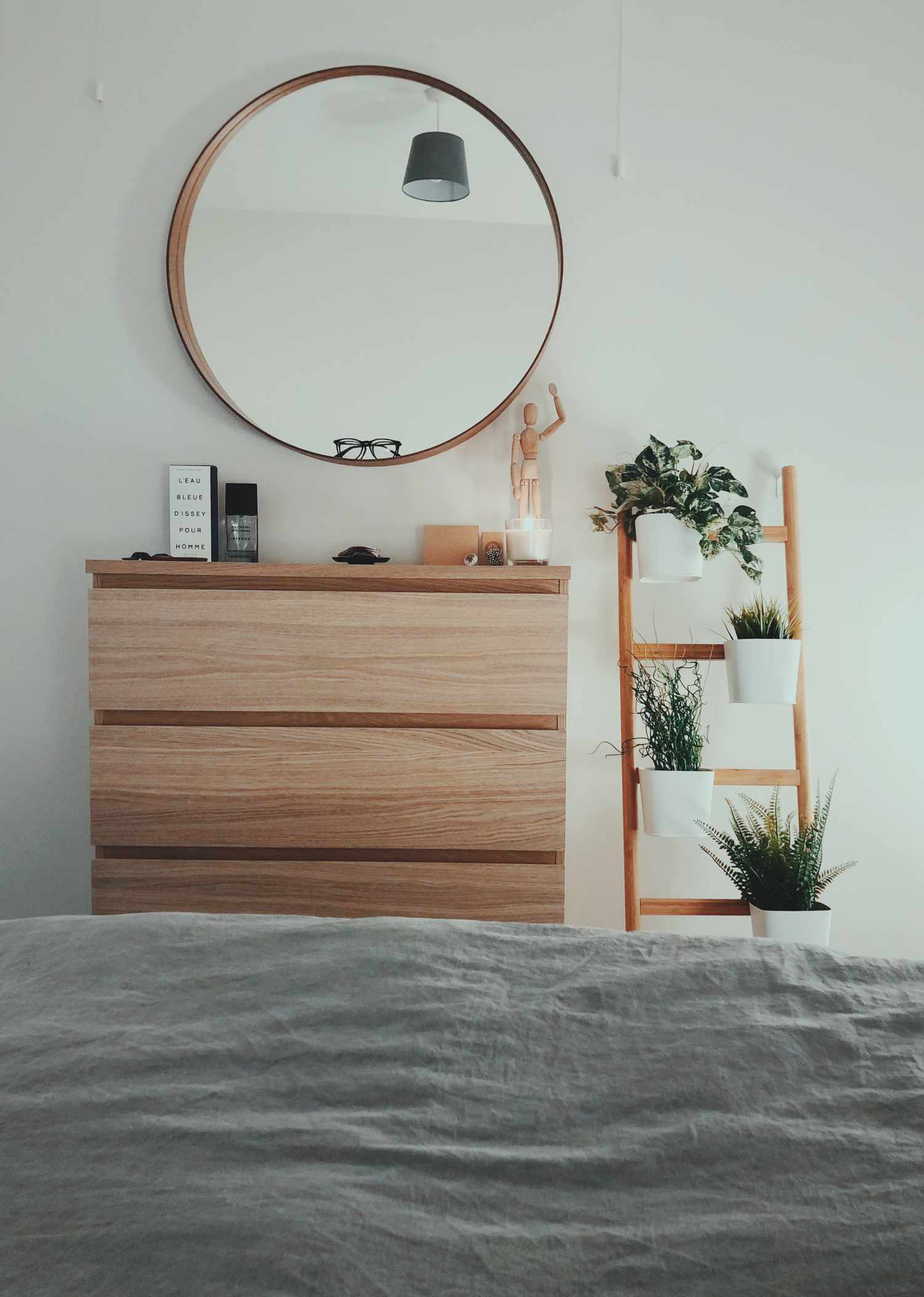 dormitorio con plantas, cómoda y un espejo redondo