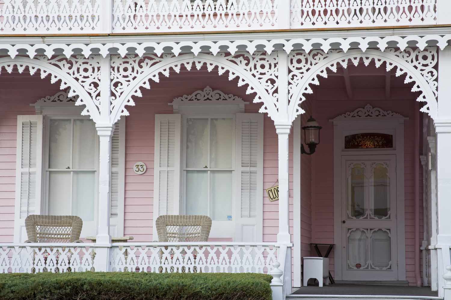 Detalle de porche ornamentado en blanco, contraventanas blancas, revestimiento de la casa rosa