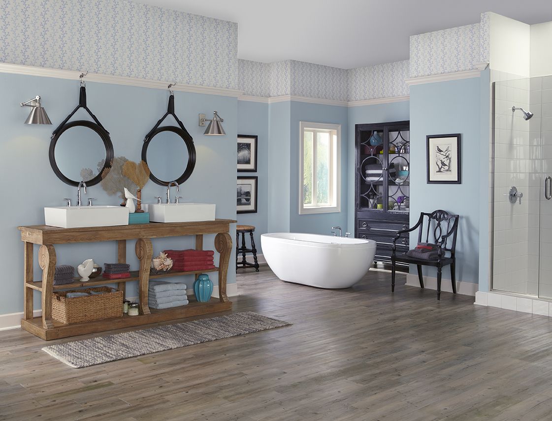 Ein Badezimmer mit Tapetenakzenten an der Decke, Holzböden, einer separaten Badewanne und hölzernen Waschtischen mit Landhauswaschbecken.