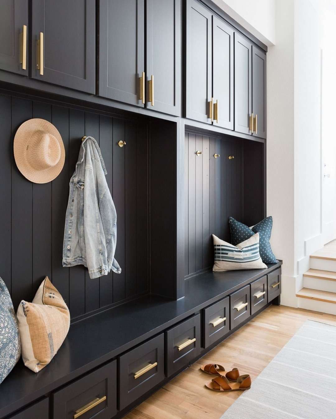 Un gran mudroom con almacenaje en azul marino, ganchos de latón y cojines decorativos.