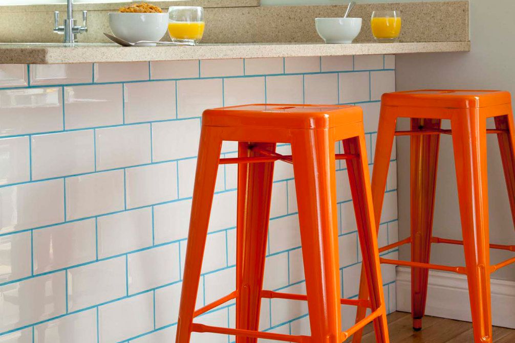 Comptoir de cuisine avec joint turquoise sur carrelage métro blanc, avec deux tabourets de bar orange
