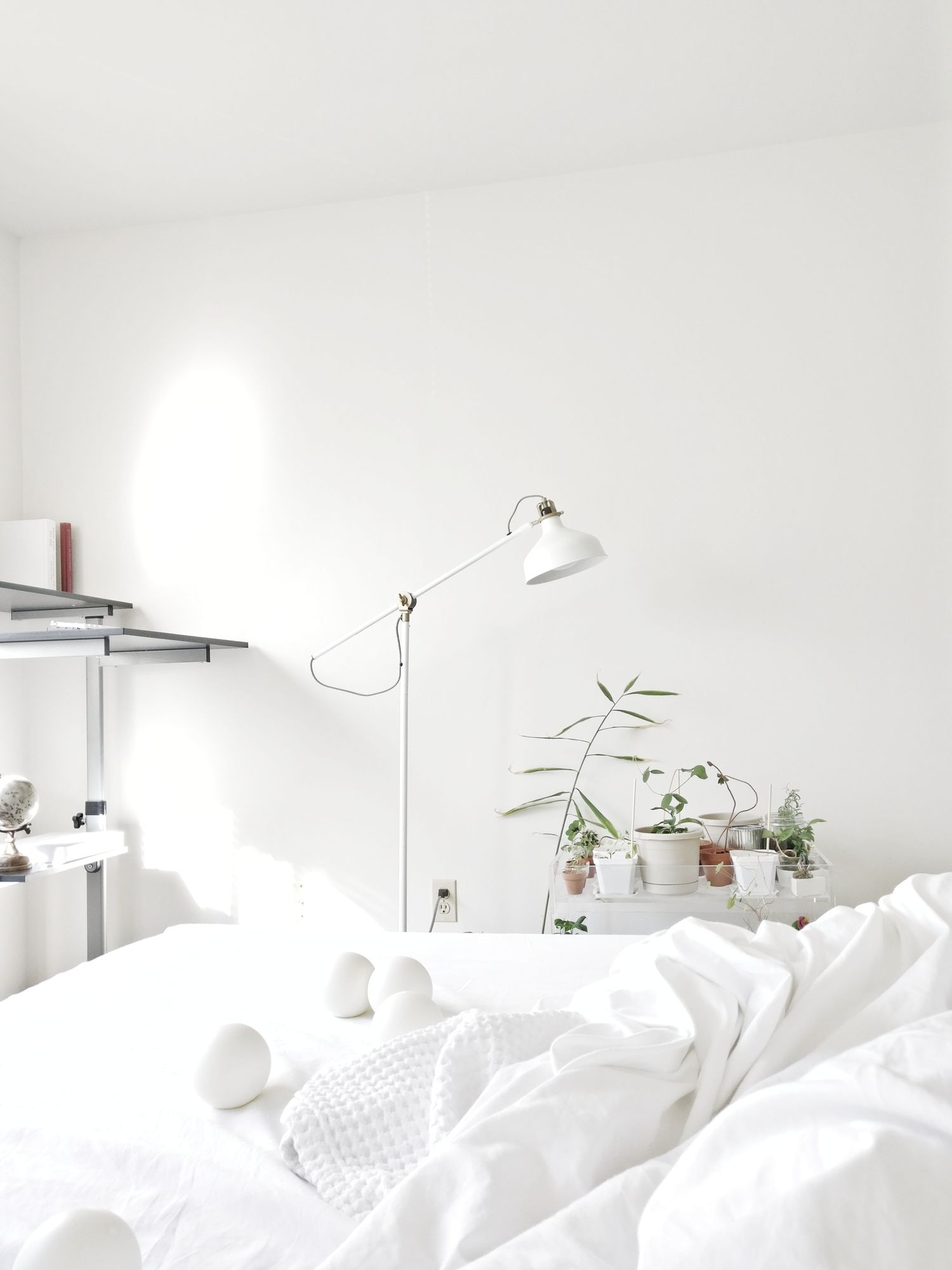 weißes Schlafzimmer mit Pflanzen, Lampe und weißer Bettwäsche