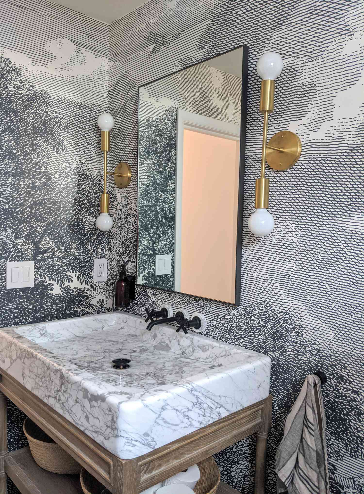 Une salle de bain dans la maison de Molly et Fritz à Shaker Heights présente un traitement graphique des murs, un évier rectangulaire en marbre, une quincaillerie noire et un éclairage en laiton
