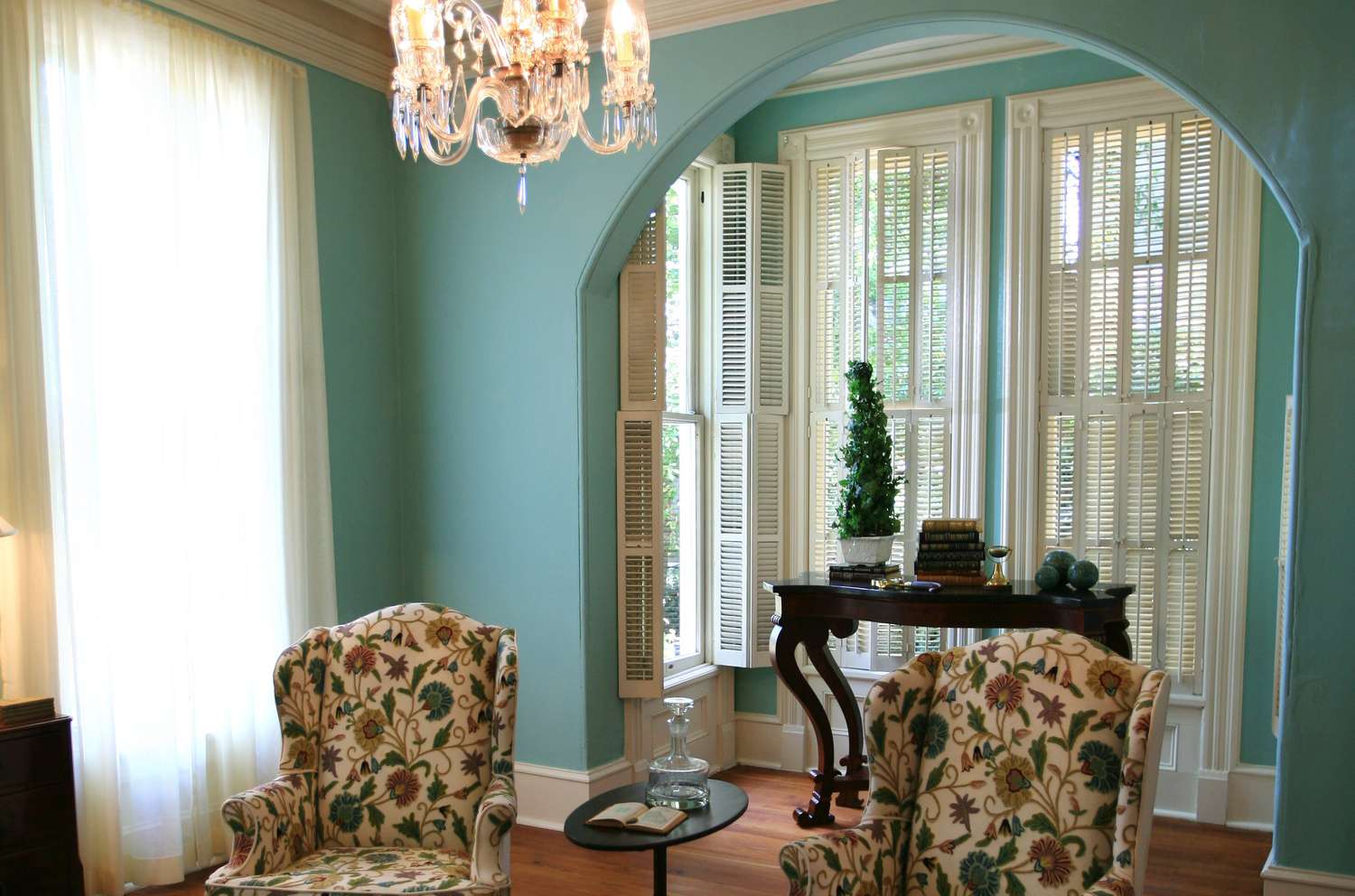 Pared de color azul verdoso con recorte en arco con ventanas de suelo a techo en extensión de cuatro paredes poco profundas -- muebles de época y suelos de madera