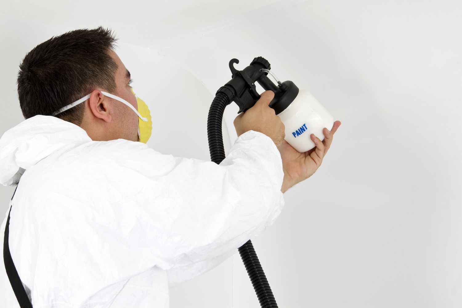 Pintor pulverizando pintura sobre pared blanca