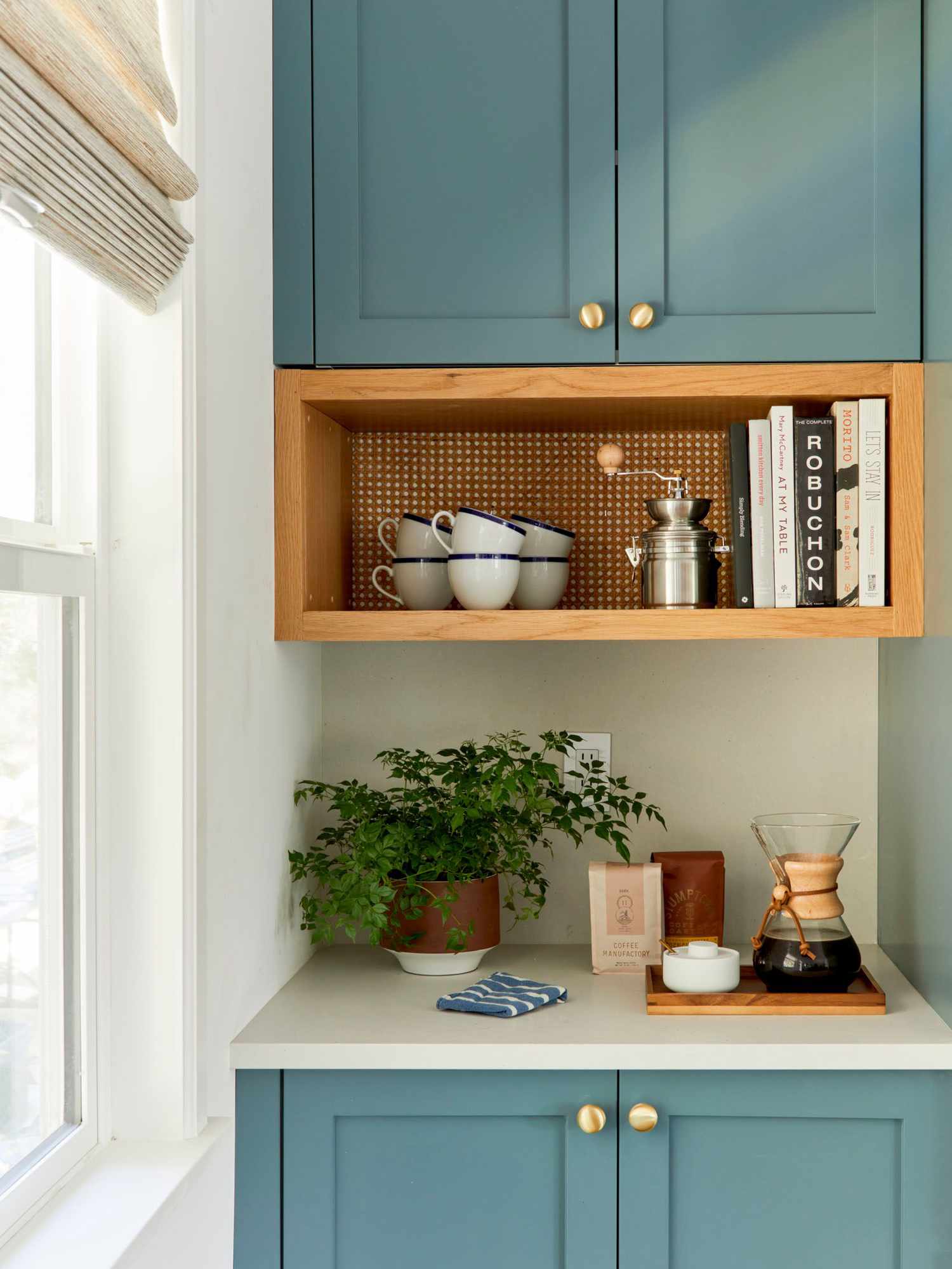 estación de bebidas con armarios azules, estante de madera incorporado con tazas y libros de cocina