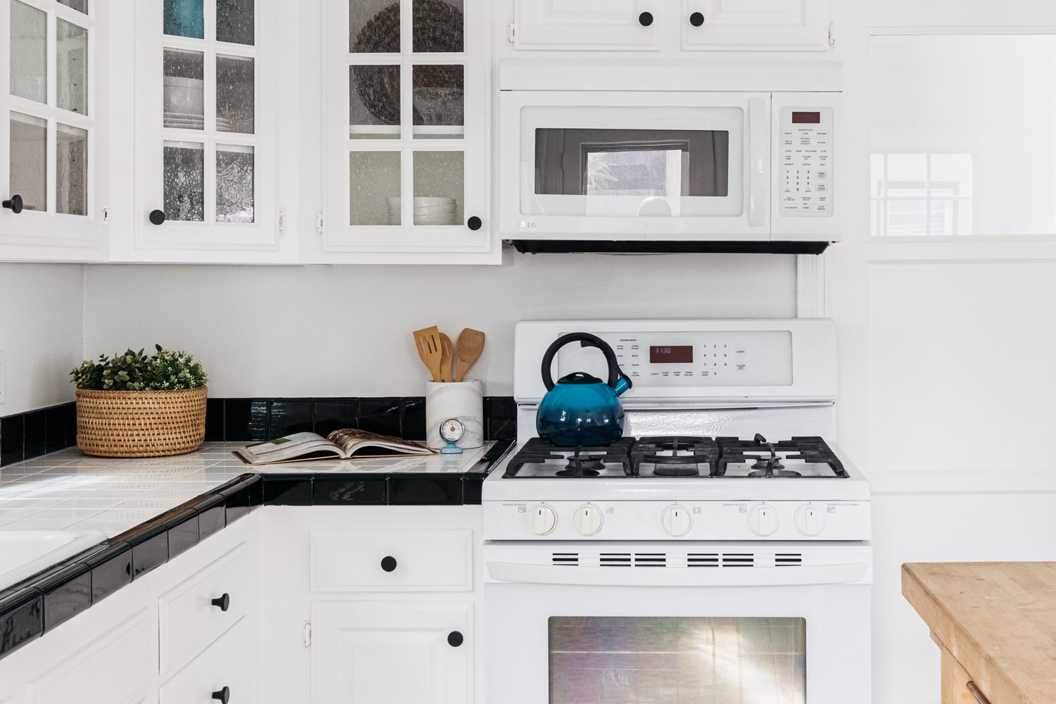 Moderne Küche mit komplett weißen Schränken und Geräten mit hellem Dekor auf schwarzen und weißen quadratischen Fliesen