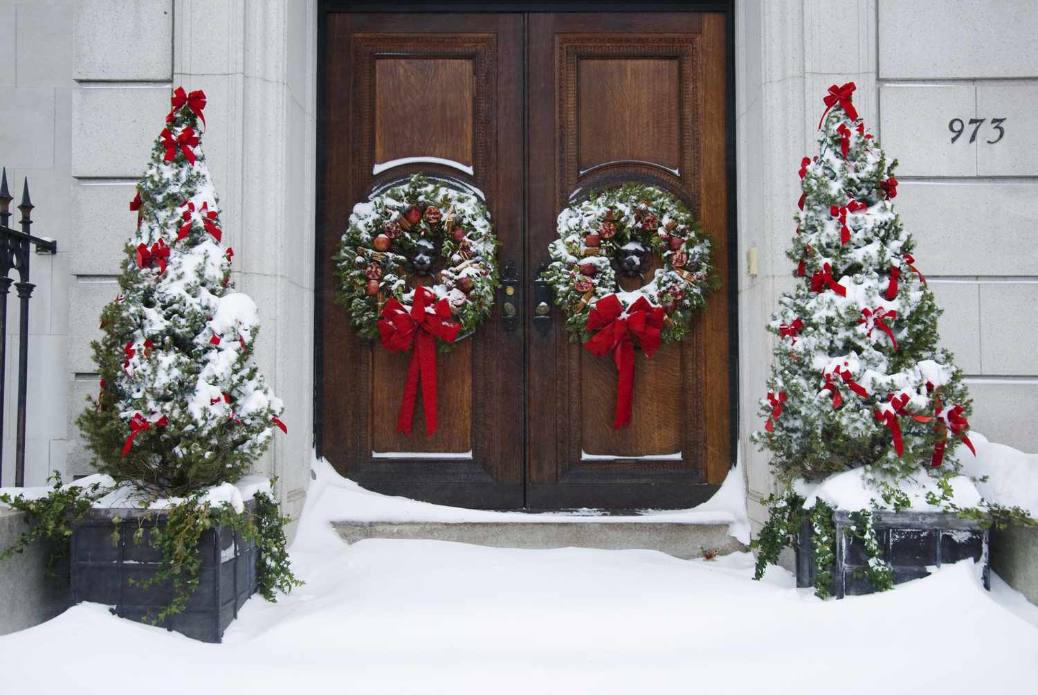 Abetos de Alberta decorados para Navidad y flanqueando una puerta principal con coronas.