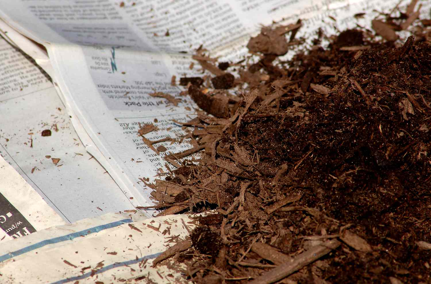 Zeitungspapier (Bild) kann Ihren Rasen ersticken. Tragen Sie Mulch auf, um es zu beschweren.