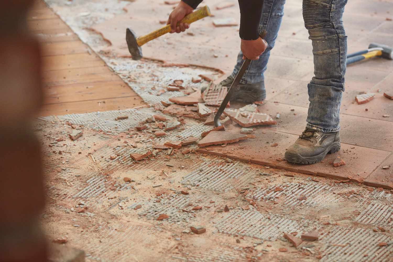 Ladrilhos de piso de cerâmica sendo removidos manualmente com um cinzel de alvenaria e um raspador de piso