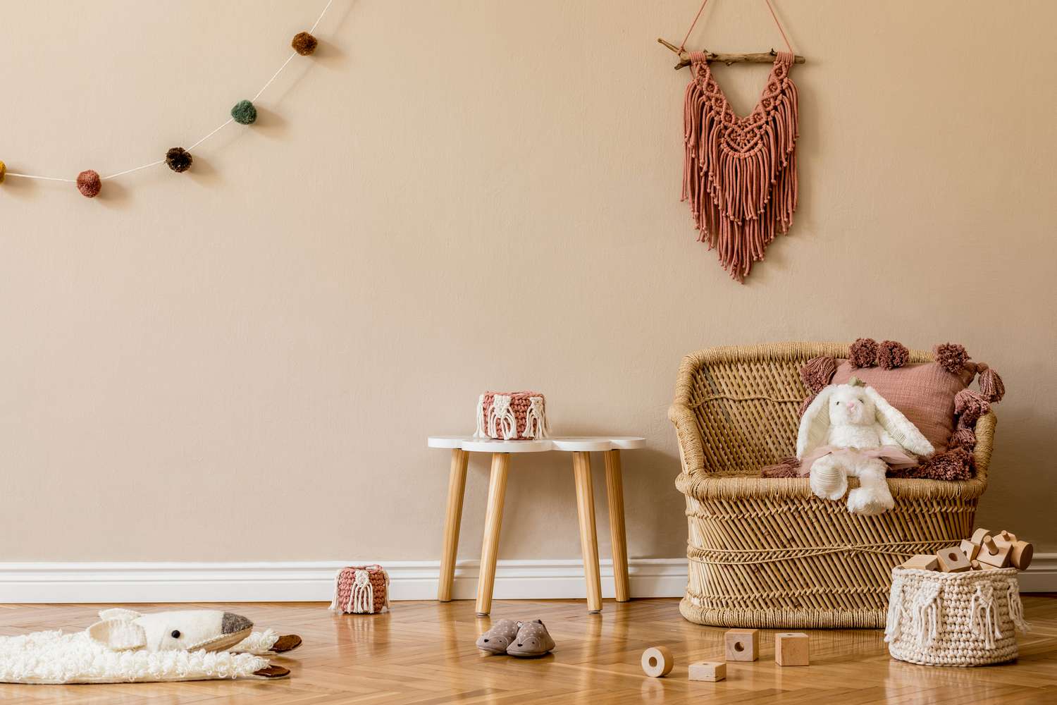 Stilvolle und niedliche skandinavische Dekoration eines Neugeborenen-Babyzimmers mit Naturspielzeug, hängenden Dekokugeln, Makramee, Pouf, Plüschtieren und Teddybären. Beigefarbene Wände. Inneneinrichtung eines Kinderzimmers. Home Staging.