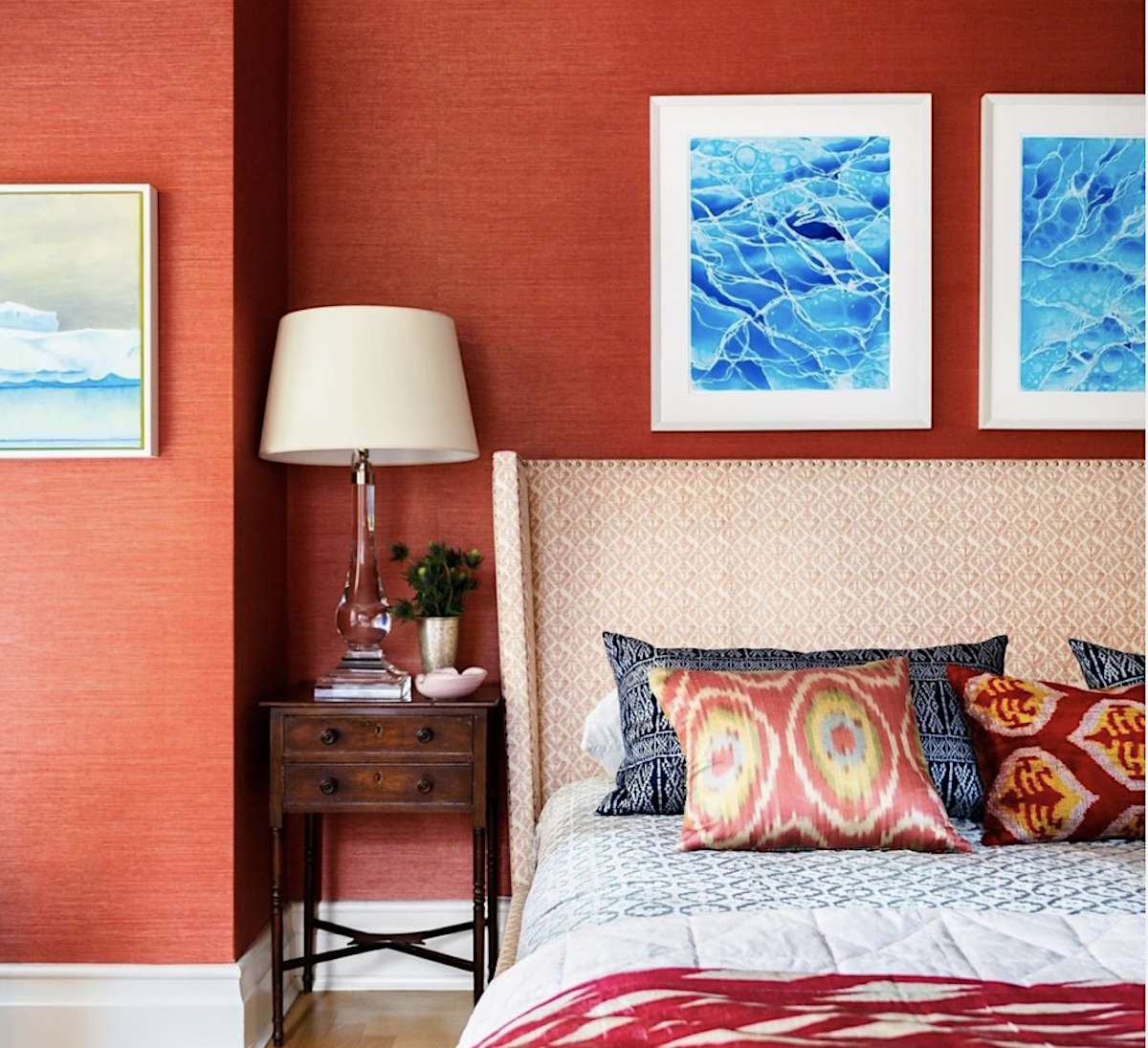 quarto vermelho com estampas oceânicas sobre a cama, cabeceira com padrão branco, criado-mudo de madeira escura