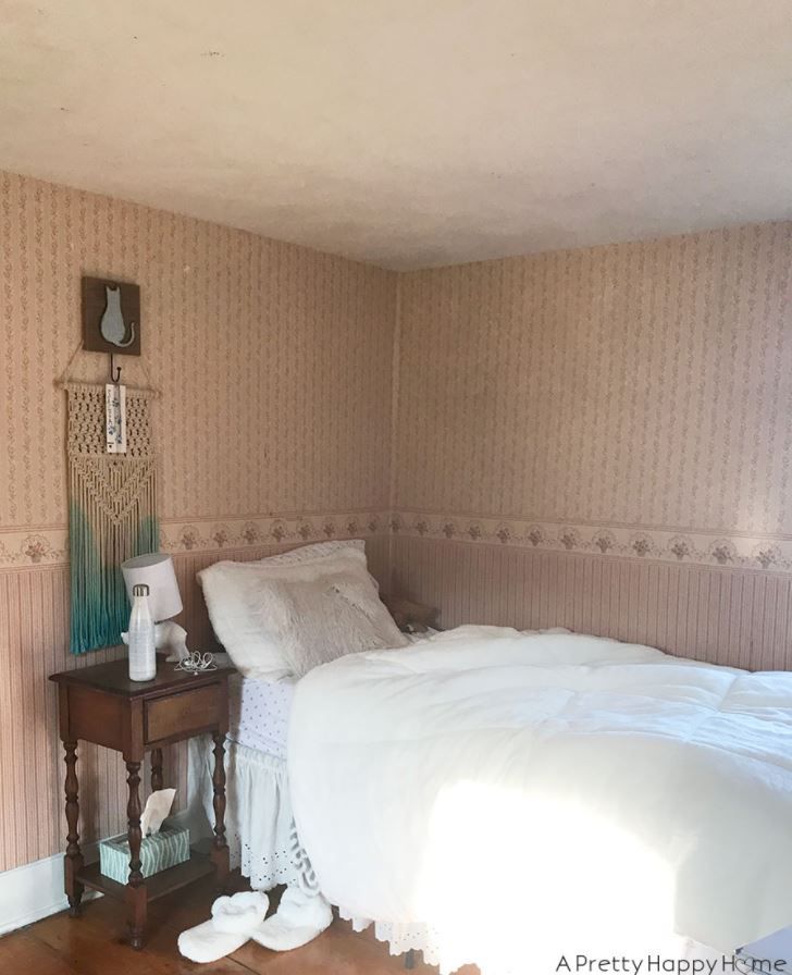 Girl's bedroom with muted pink wallpaper and white bedding.