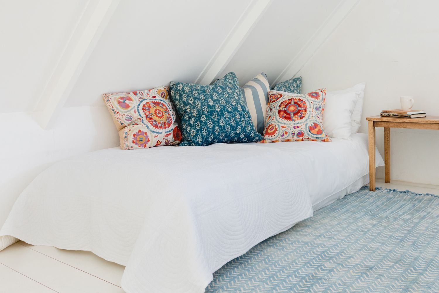 Cama de chão portátil coberta com uma capa de cama branca e travesseiros azuis e laranja em cima