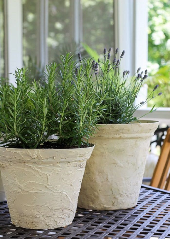 Dois vasos de pedra envelhecida com ervas plantadas em seu interior.