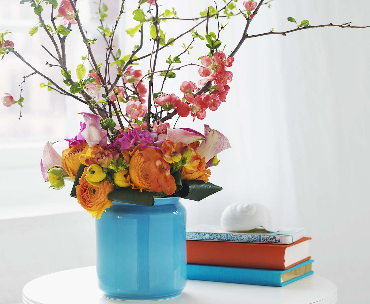 Jarrón azul sobre una mesa con flores de colores junto a tres libros.