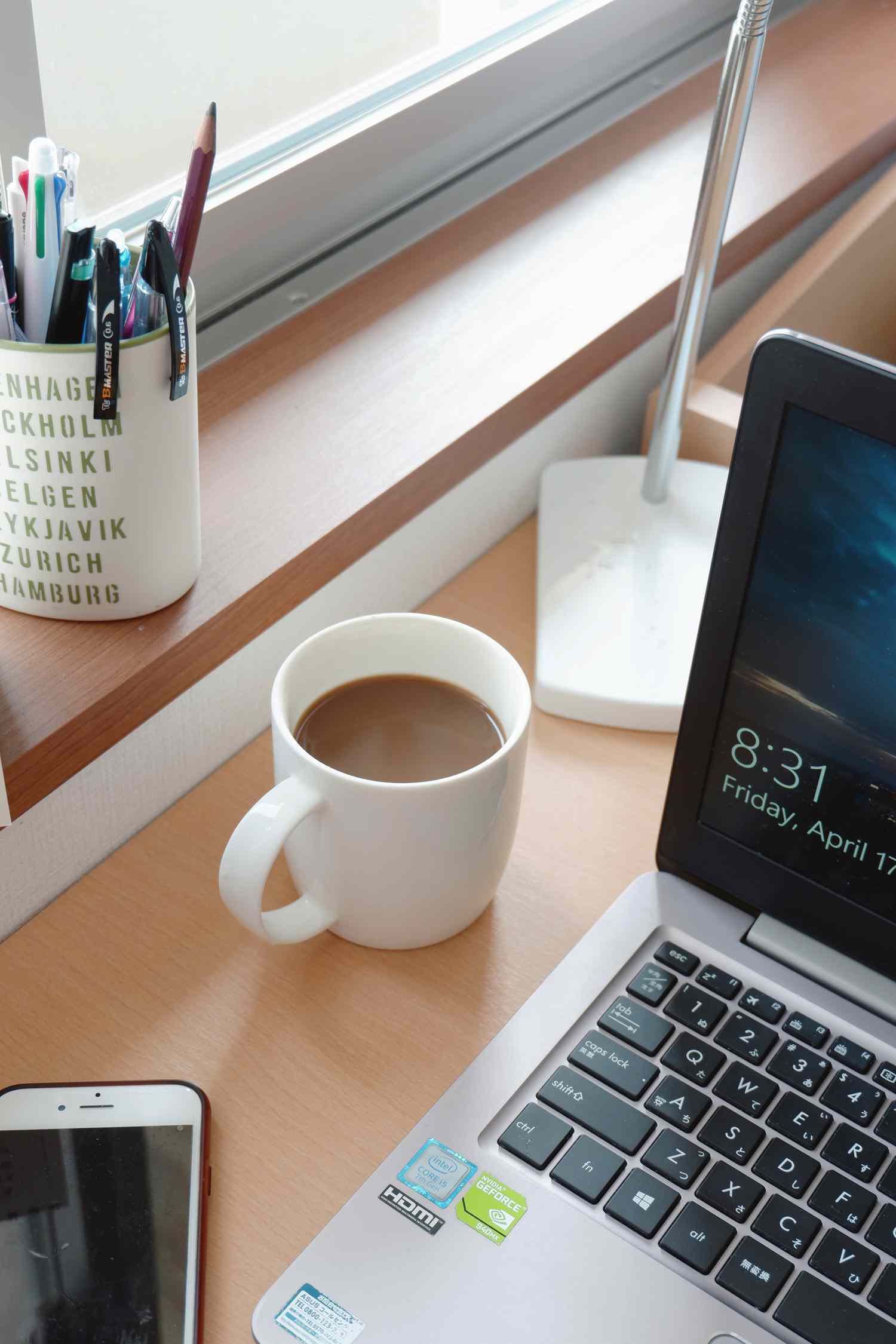 mesa com laptop, lápis, telefone celular e xícara de café