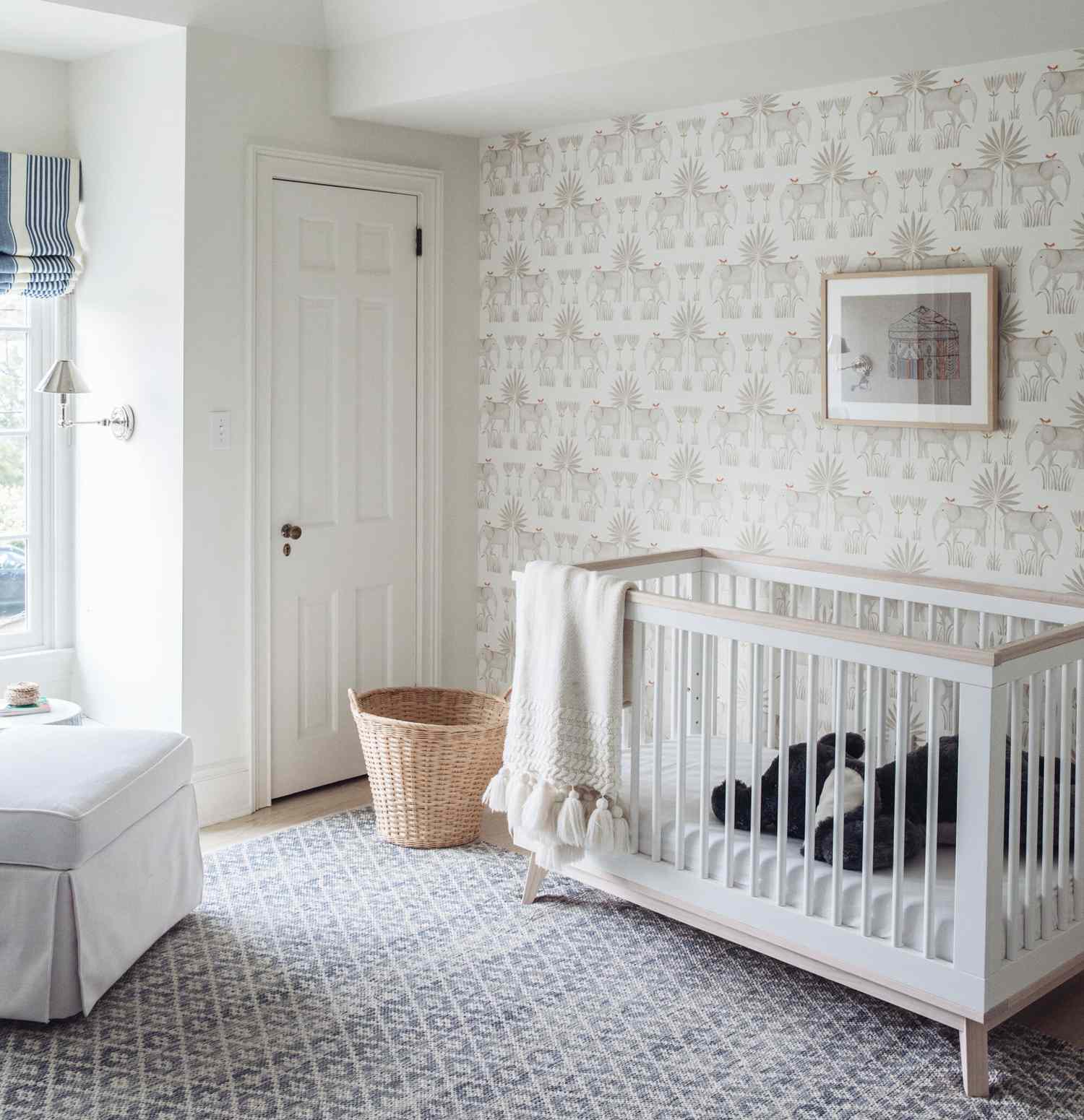 nursery with white color scheme, elephant print wallpaper, wicker basket between crib and closet door