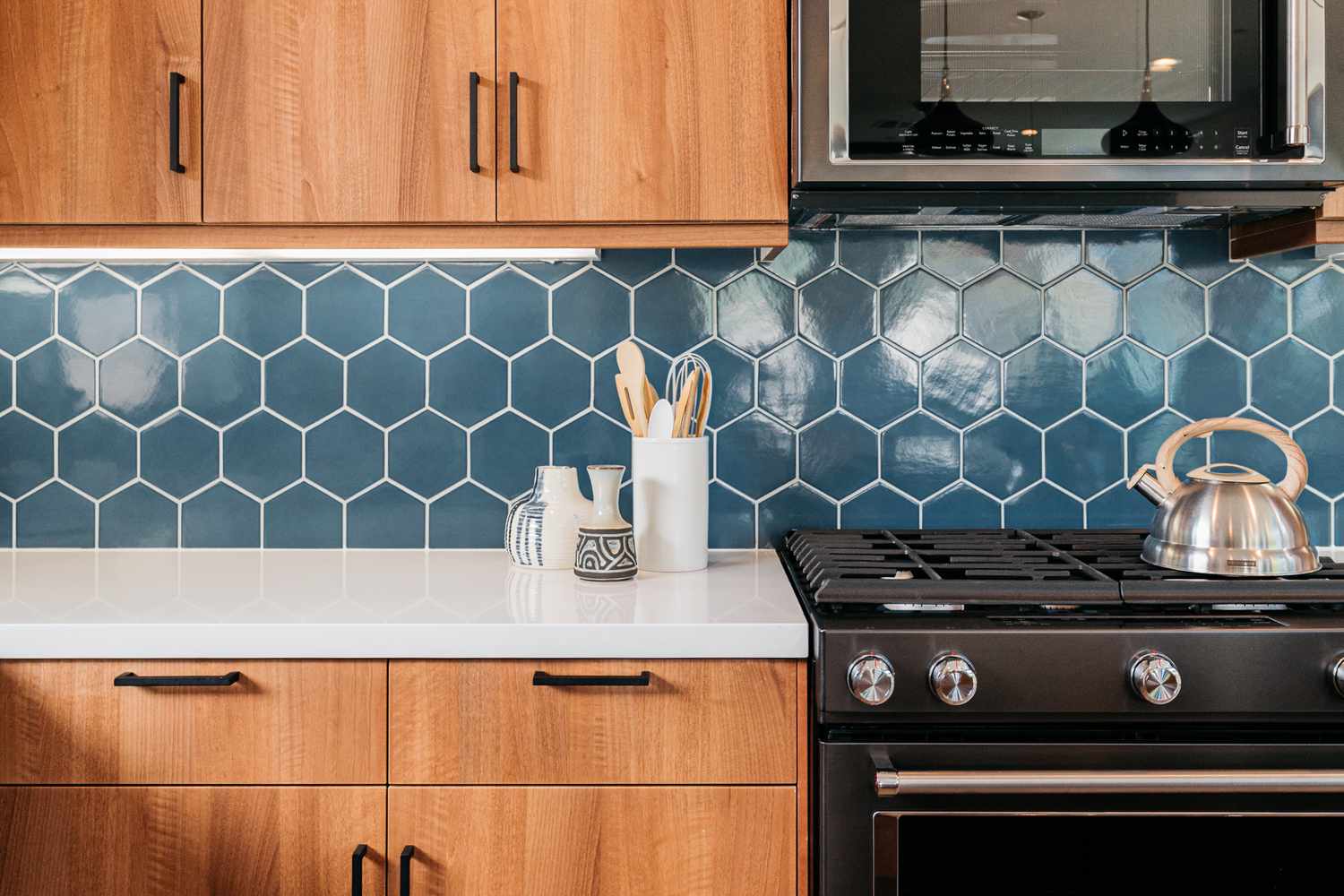 Blaue geometrische selbstklebende Fliesenmatte in Küche mit Holzschränken und schwarzen Geräten