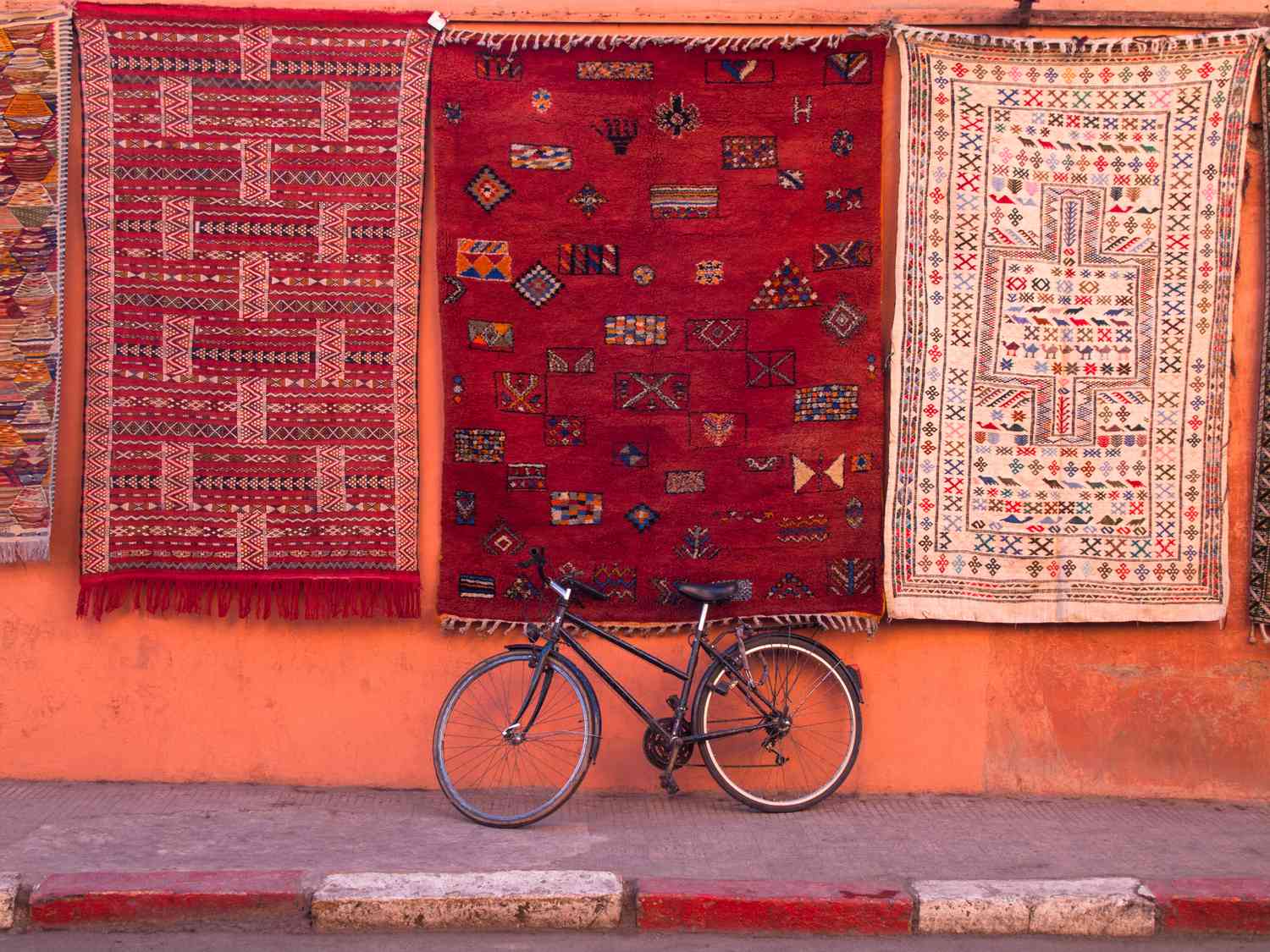 Bicicleta aparcada en la pared bajo alfombras colgantes con motivos tradicionales.