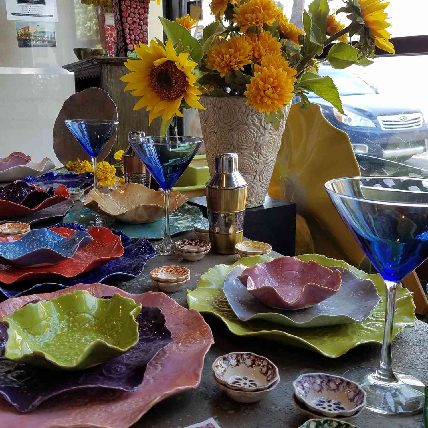 Bunte Tischdekoration mit blauen Martini-Gläsern, mehrfarbigen Tellern und Schalen mit Blumenrand und einem gelben Blumen-Mittelstück