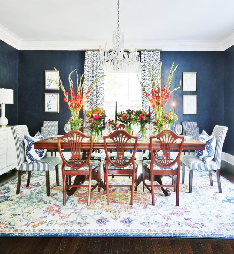 Sala de jantar com paredes azuis escuras e grandes buquês de flores sobre a mesa.