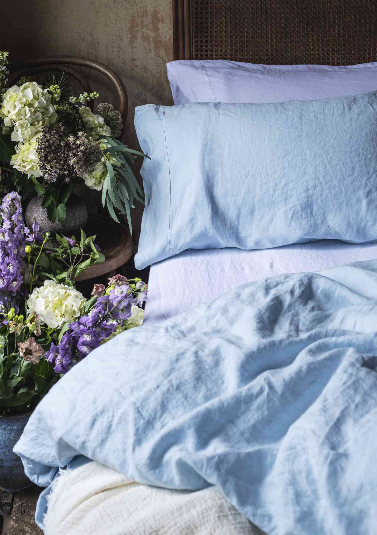 Roupa de cama de linho azul lago do Leitão ao lado de flores brancas e roxas