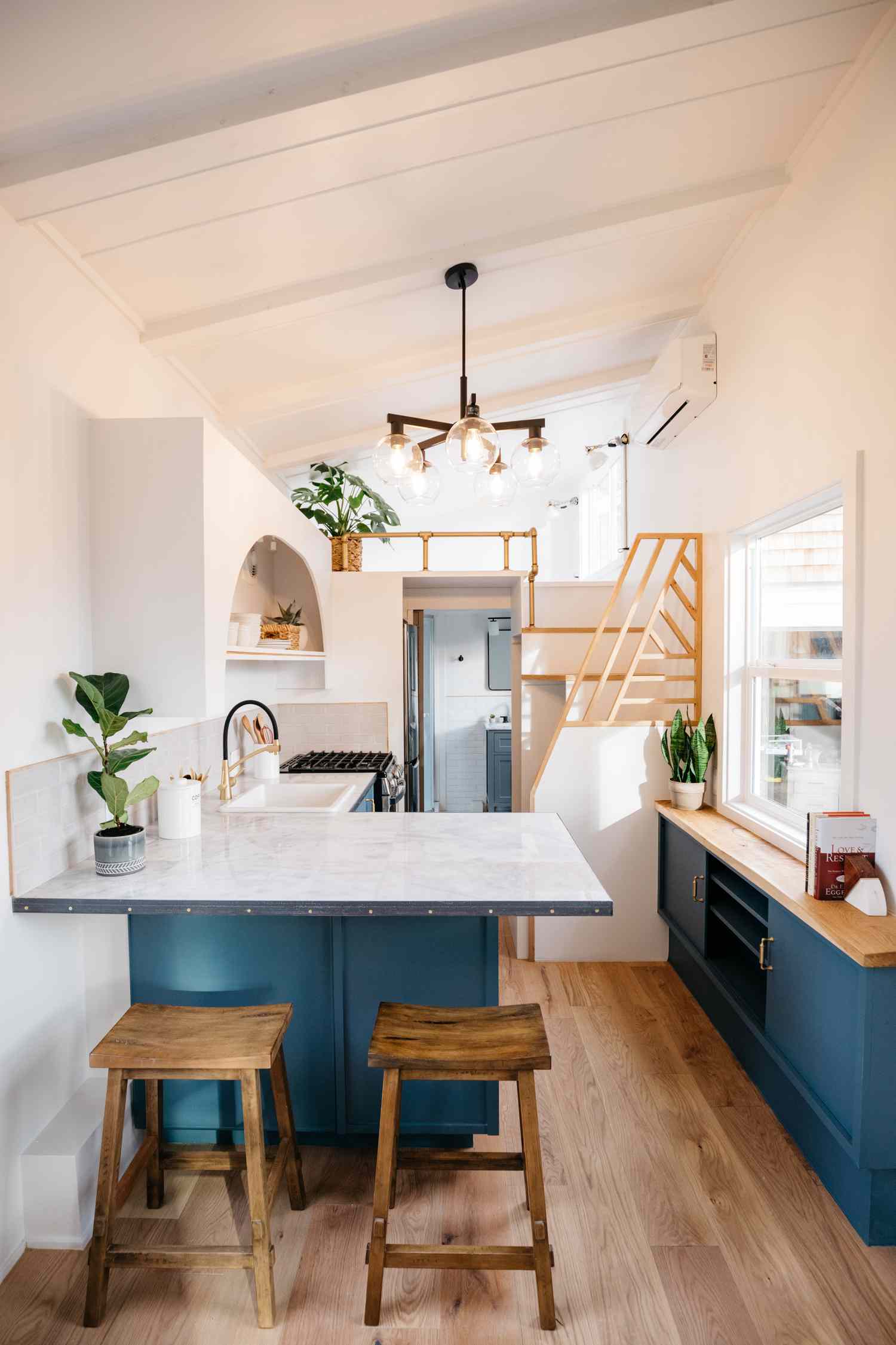 cozinha de casa minúscula com armários azuis, escada geométrica e bancadas brancas