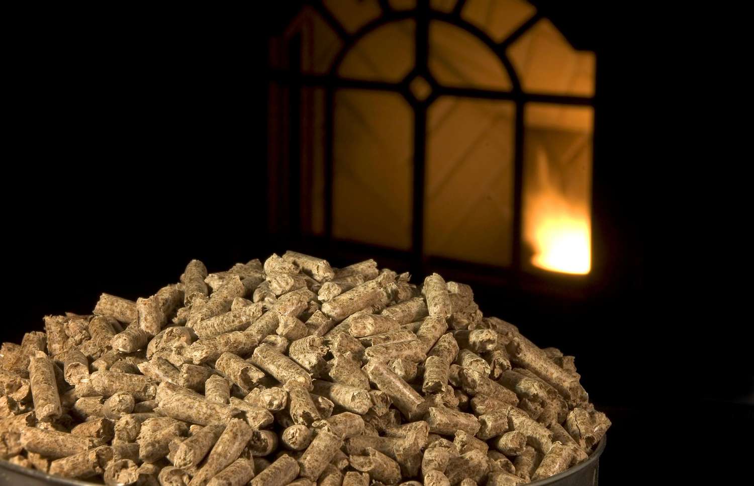 Holzpellets mit beleuchtetem Pelletofen im Hintergrund