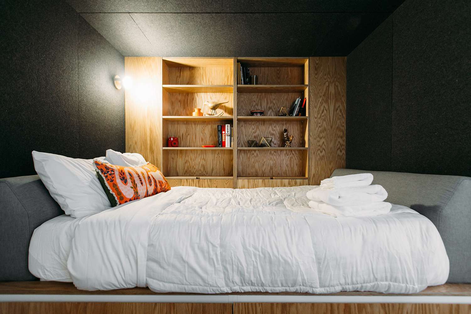 tiny dark grey bedroom with plywood storage wall