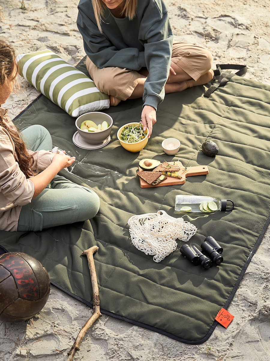 zwei Mädchen beim Picknick auf armeegrüner Picknickdecke im Sand