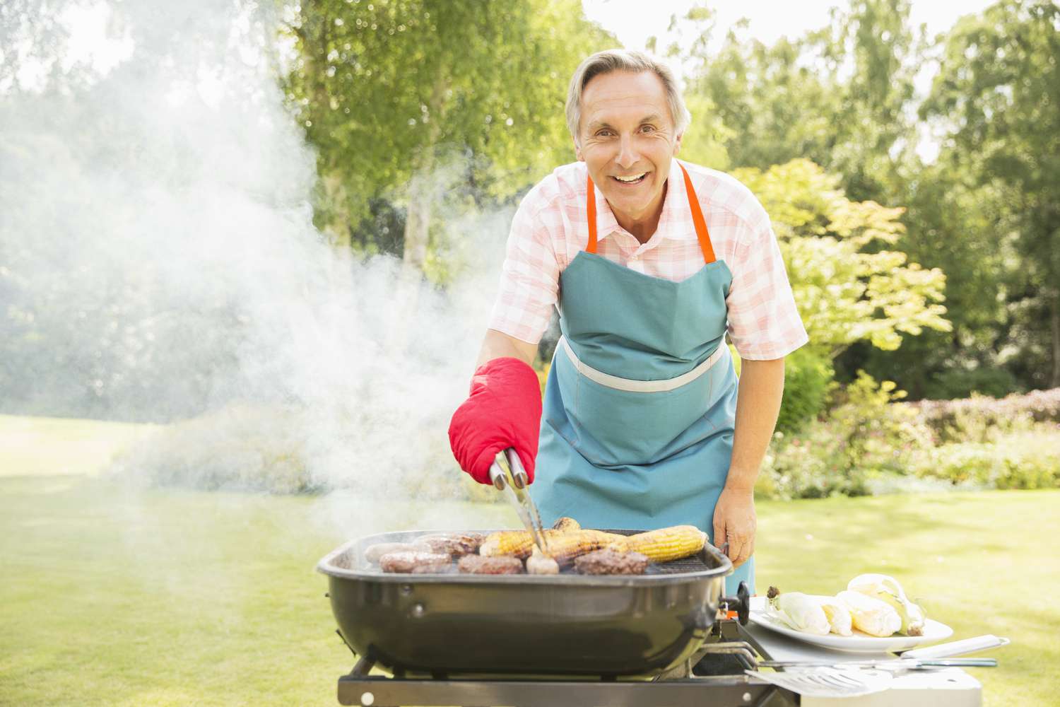 Principal con delantal y guante de cocina asando comida en una parrilla.