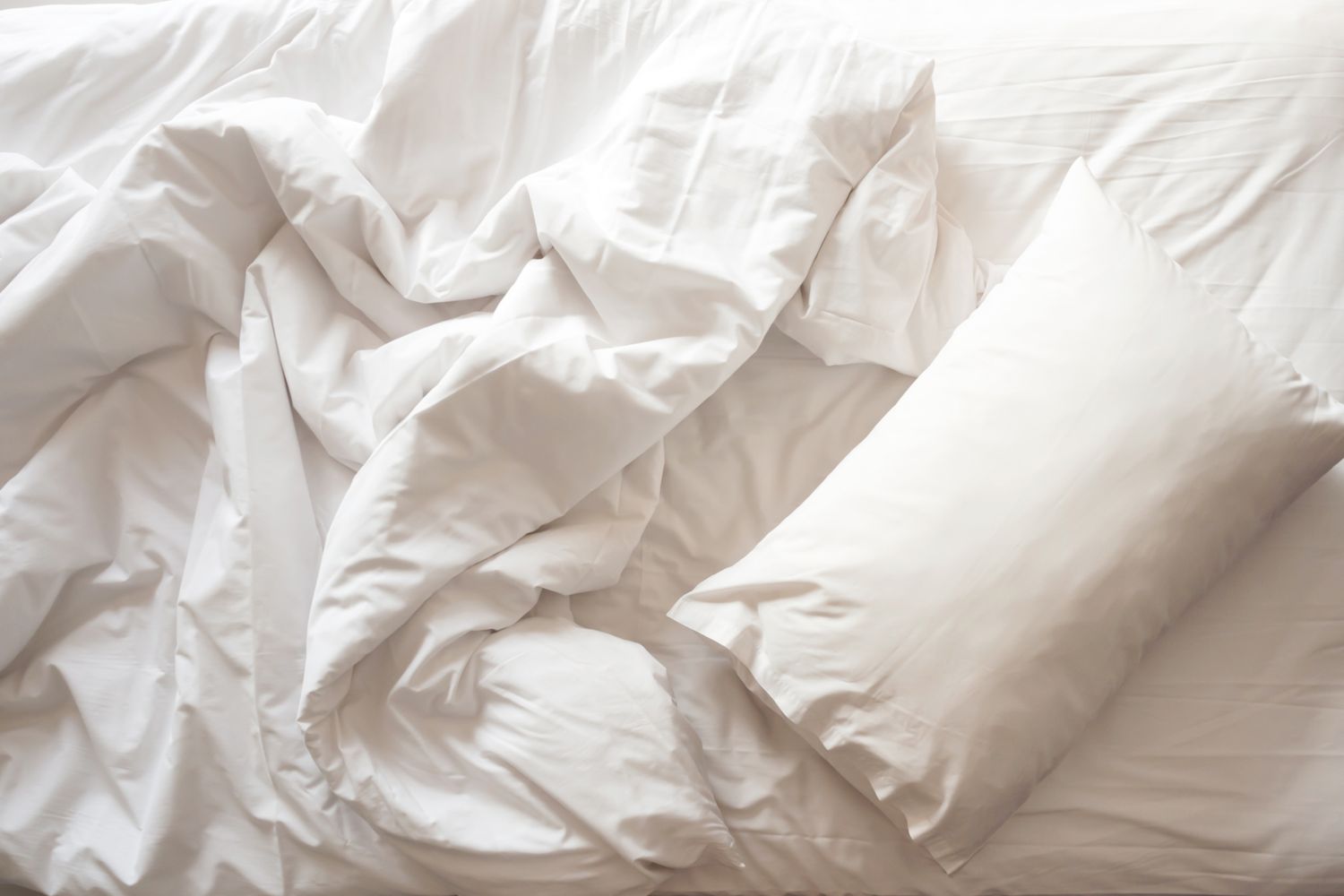 Ein weißes Kissen auf einem unordentlichen weißen Bett.