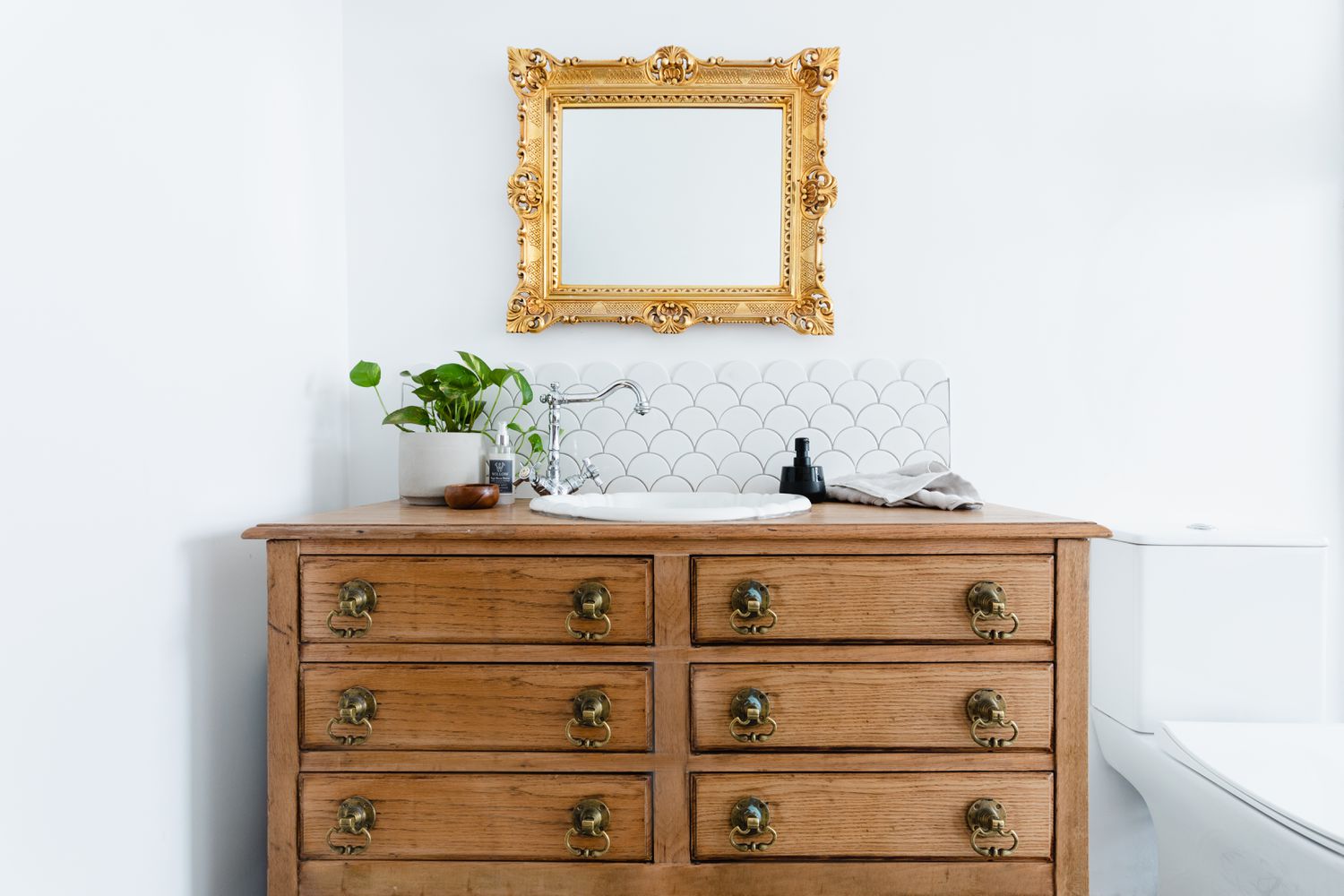 Upcycled tocador de madera utilizado en el baño como lavabo por debajo de oro espejo enmarcado